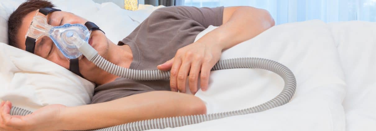 asian-man-wearing-cpap-mask-connecting-to-air-hose-sleeping-on