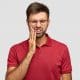 photo-of-caucasian-man-suffers-painful-toothache-has-rotten-tooth-needs-to-visit-dentist-keeps-eyes-closed-from-pain-dressed-in-casual-red-t-shirt-isolated-over-white-background-touches-cheek