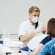 close-up-portrait-beautiful-young-lady-sitting-dental-chair-while-stomatologist-hands-sterile-gloves-holding-tooth-samples